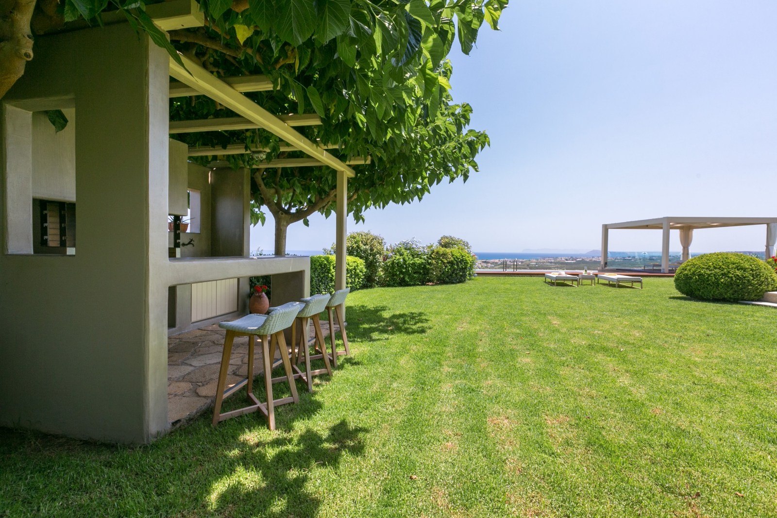Garden with grass, hedges, trees, bar and kitchen area, pool, pergola and sea view at Villa Filira on Crete, Greece