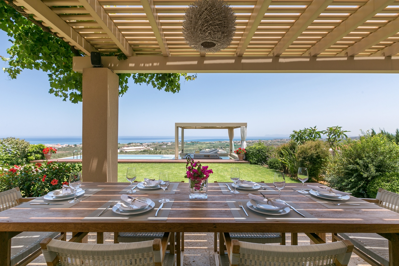 Covered outdoor dining area with table, chairs, crockery, flowers and view of pool and sea at Villa Filira on Crete, Greece