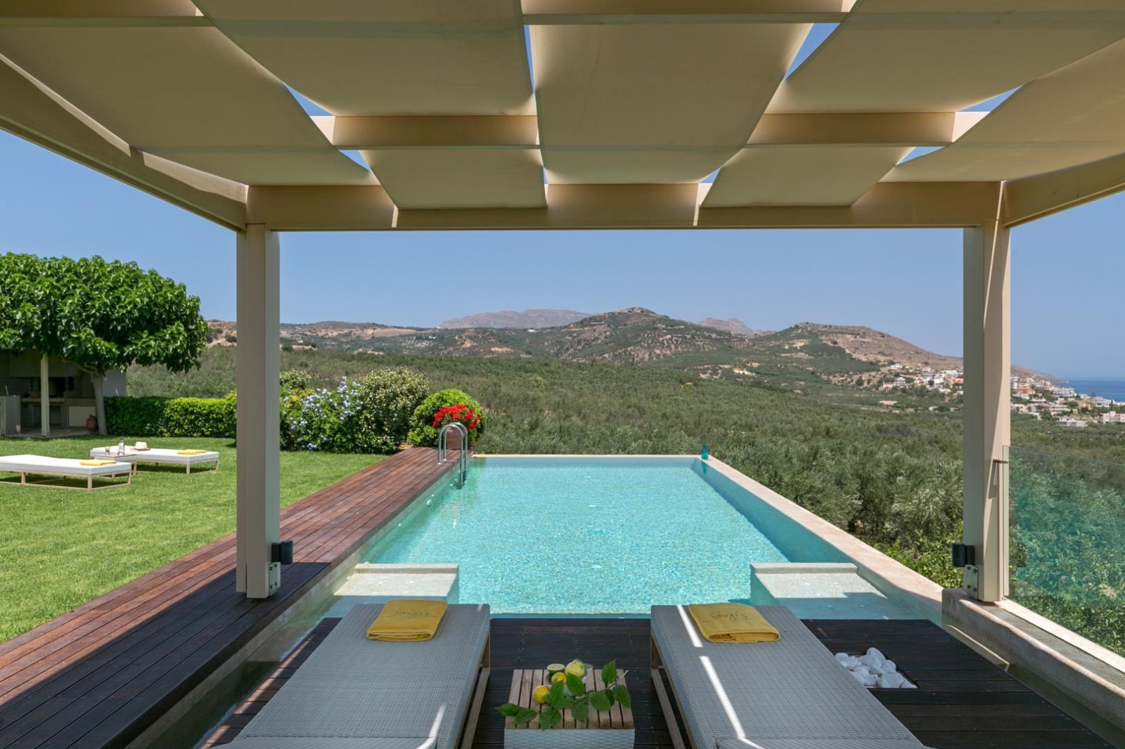 Sun loungers, towels, table and fruit in pergola with view of pool, garden and mountains at Villa Filira on Crete, Greece