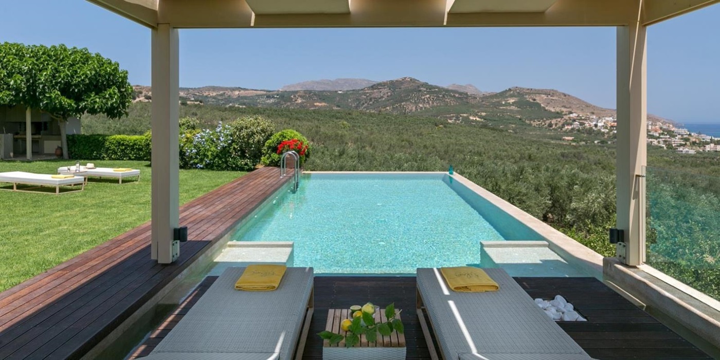 Sun loungers, towels, table and fruit in pergola with view of pool, garden and mountains at Villa Filira on Crete, Greece