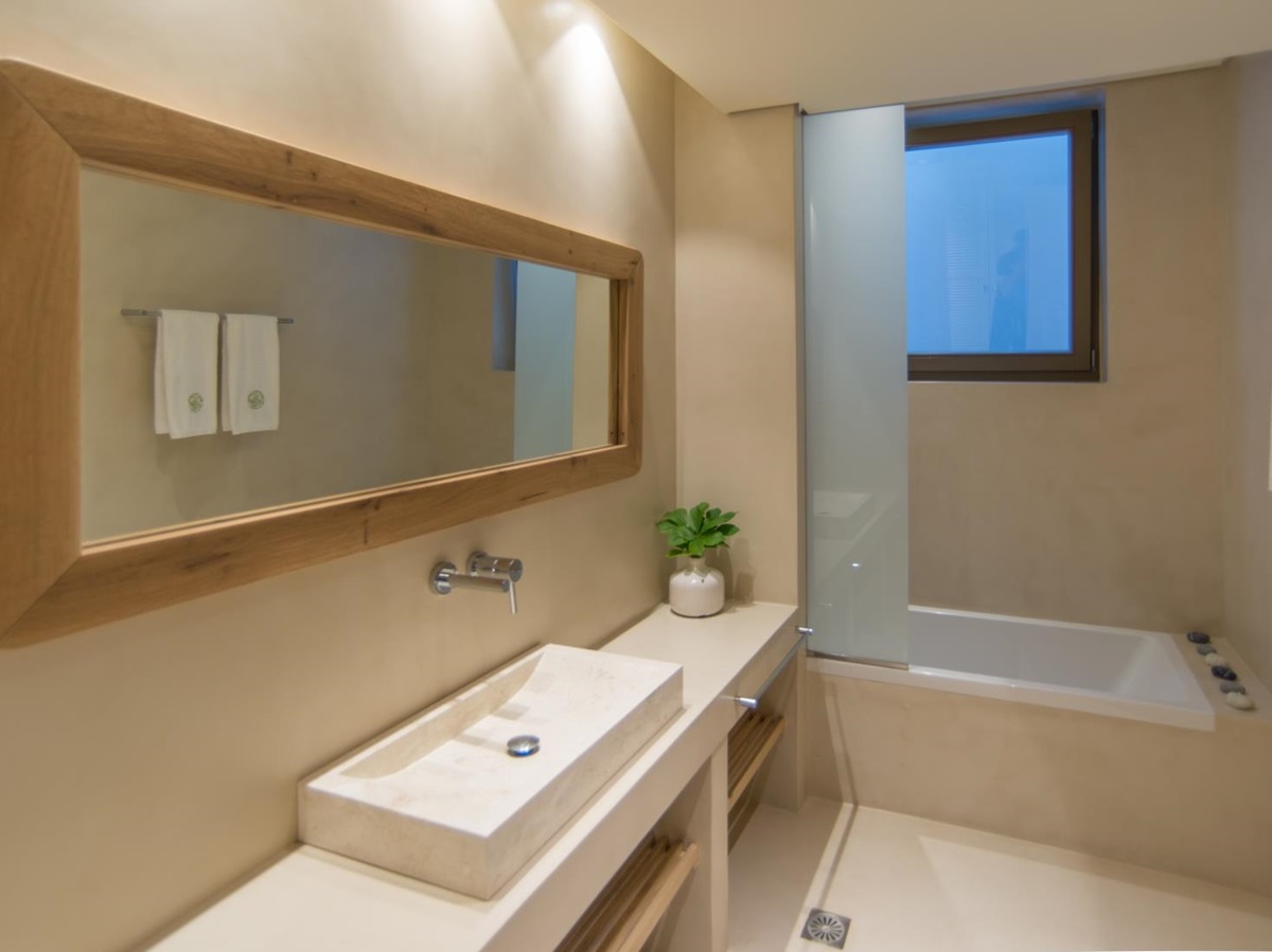 Bathroom with sink, long mirror, towel rail, plant, bath and window at Villa Ianira on Crete, Greece