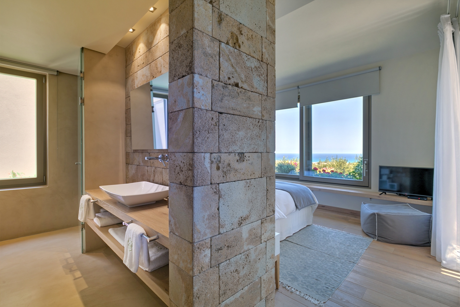 Bedroom with double bed, large windows, bean bag and TV and bathroom facilities with sink at Villa Ianira on Crete, Greece