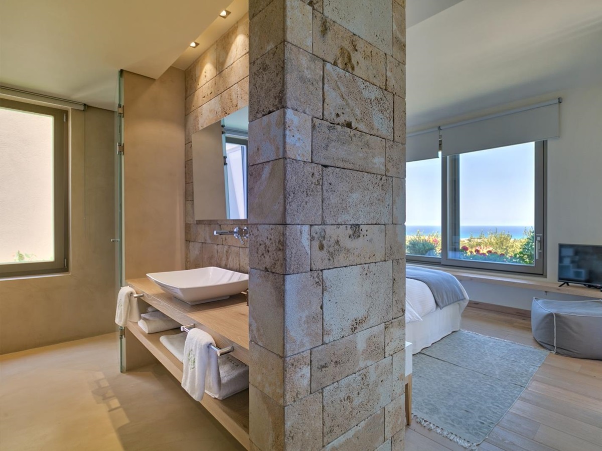 Bedroom with double bed, large windows, bean bag and TV and bathroom facilities with sink at Villa Ianira on Crete, Greece