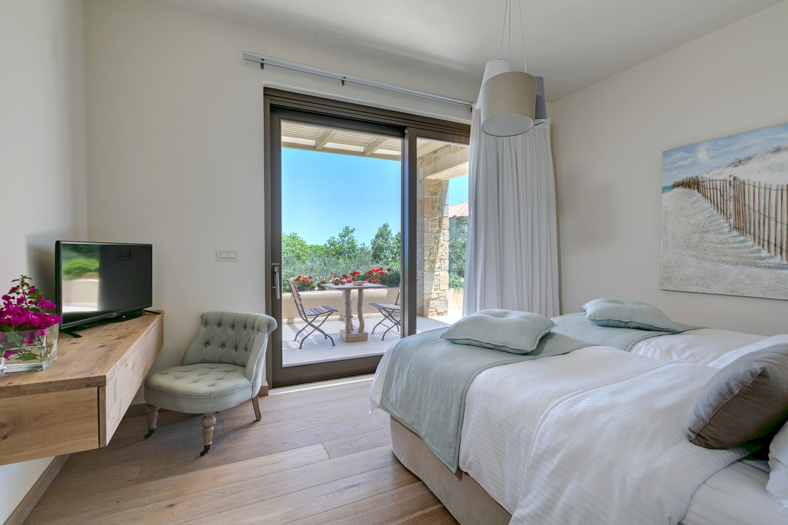 Twin bedroom with desk, flowers, armchair, TV, light, curtains and patio doors to balcony at Villa Ianira on Crete, Greece