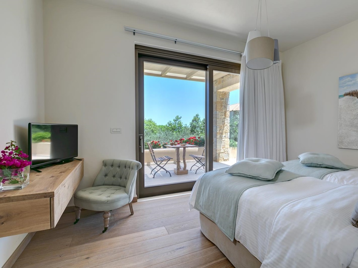 Twin bedroom with desk, flowers, armchair, TV, light, curtains and patio doors to balcony at Villa Ianira on Crete, Greece
