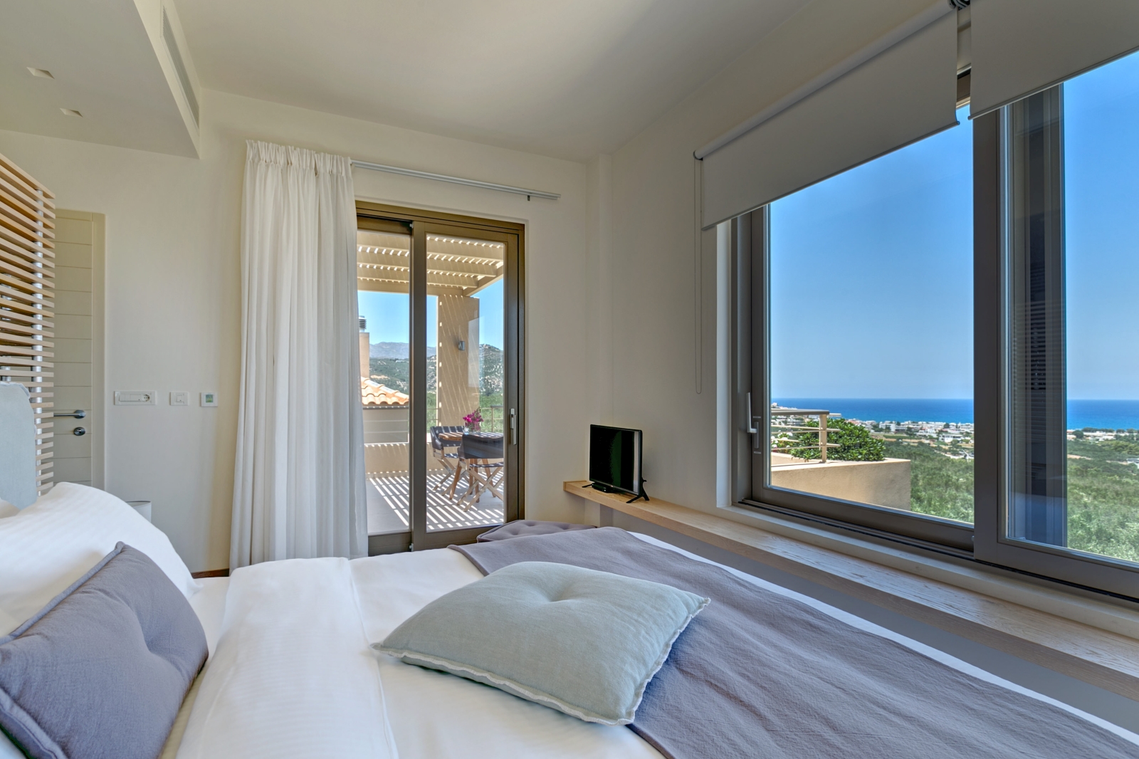 Bedroom with double bed, TV, ledge, large windows with sea view and patio doors to balcony at Villa Ianira on Crete, Greece