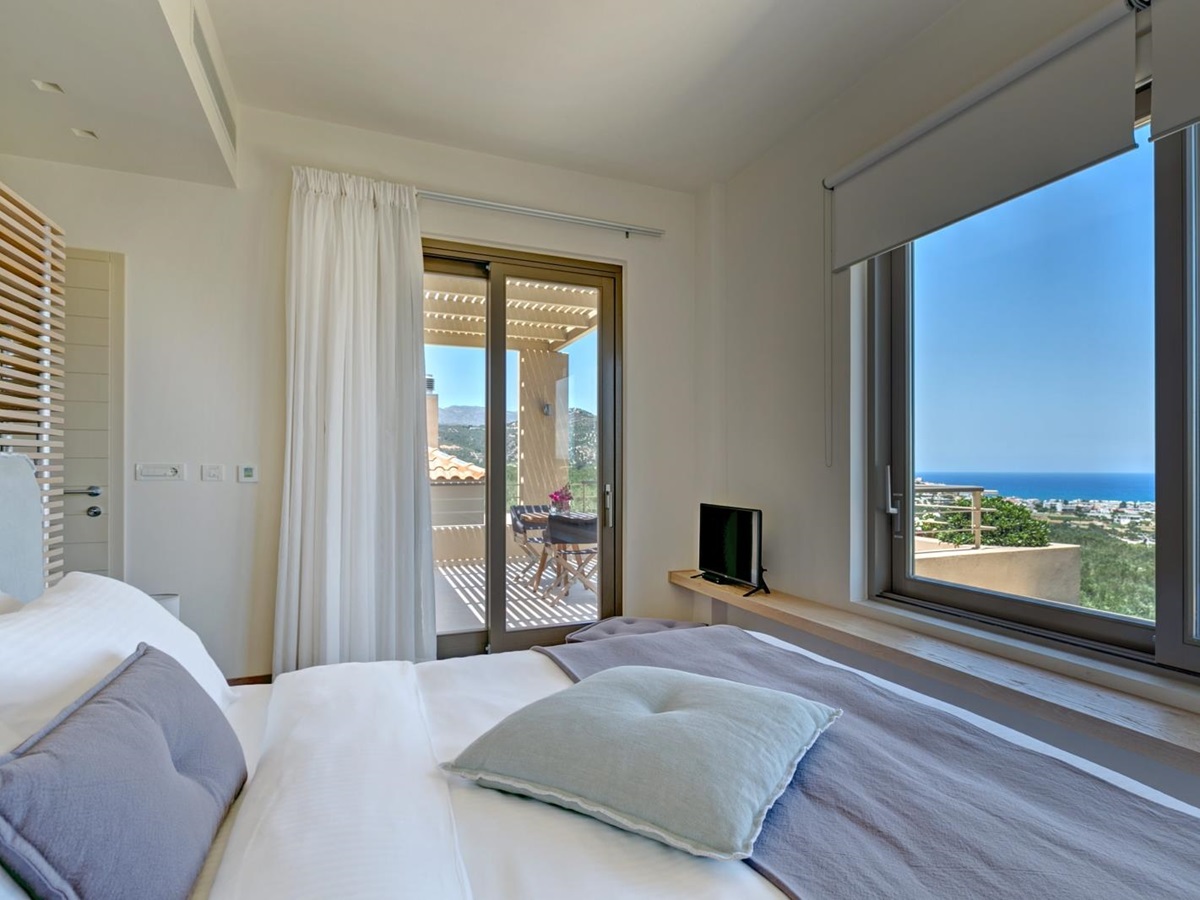 Bedroom with double bed, TV, ledge, large windows with sea view and patio doors to balcony at Villa Ianira on Crete, Greece