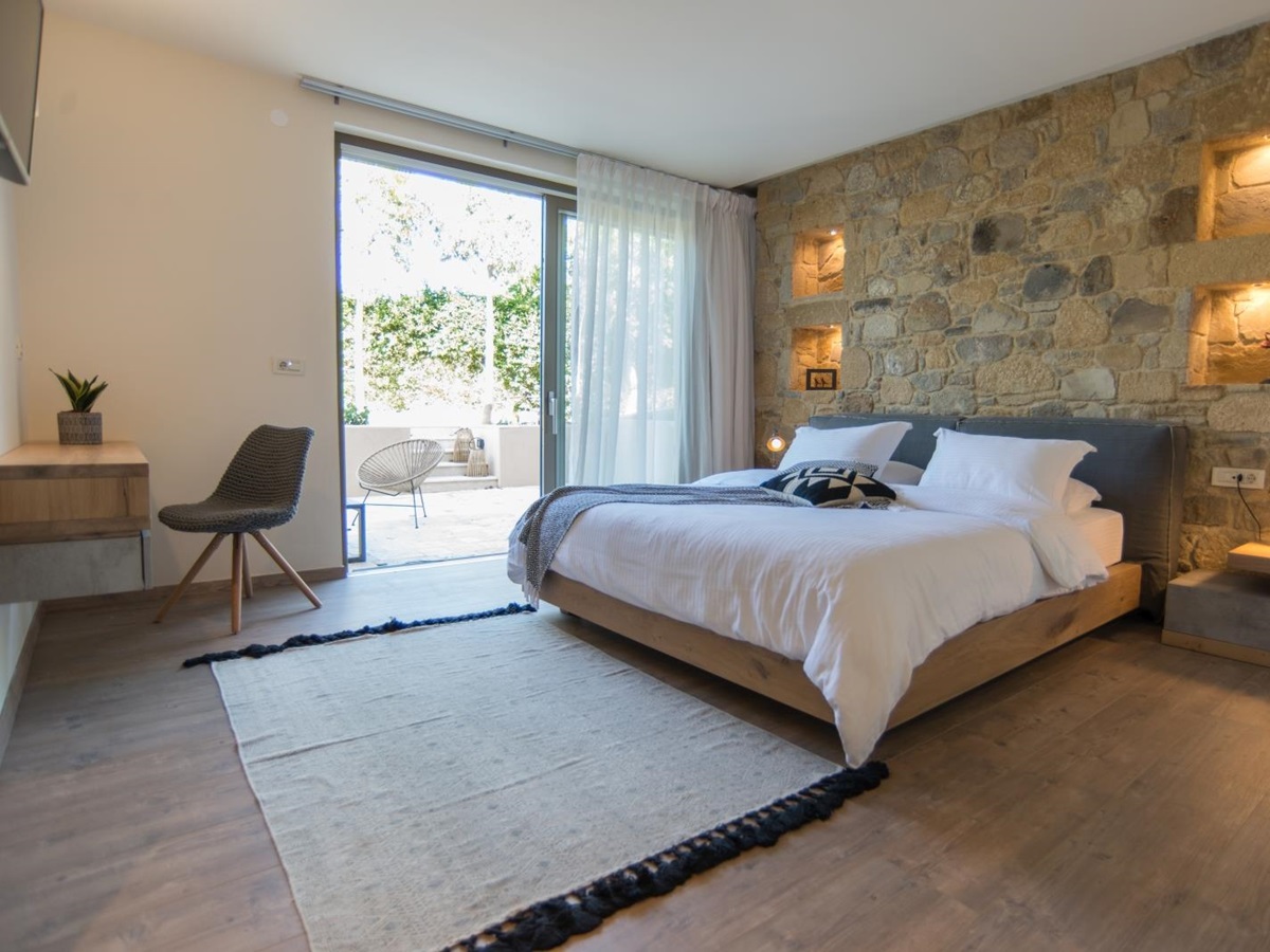 Bedroom with double bed, beside table, lamp, rug, desk, plant, armchair and patio doors at Villa Ianira on Crete, Greece