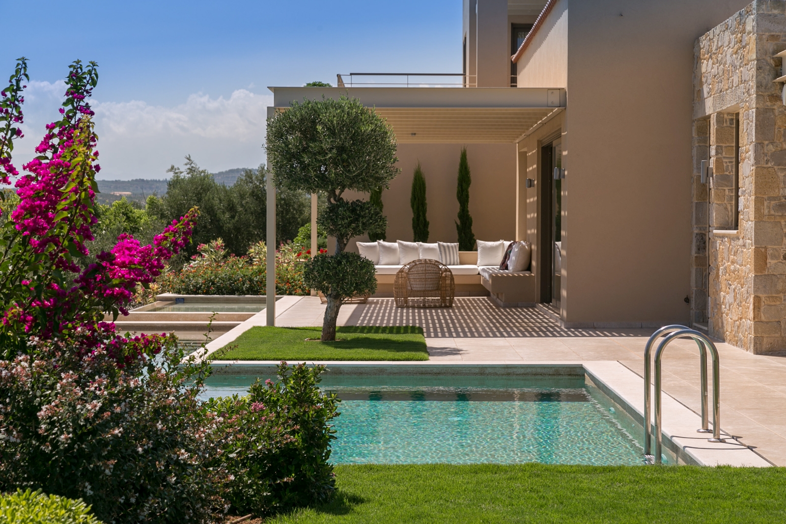 View of pool and outdoor lounge area with comfy chairs and sofa and flowers in foreground at Villa Ianira on Crete, Greece