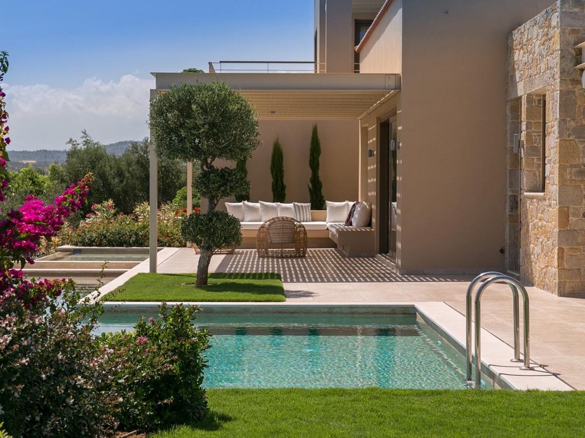 View of pool and outdoor lounge area with comfy chairs and sofa and flowers in foreground at Villa Ianira on Crete, Greece