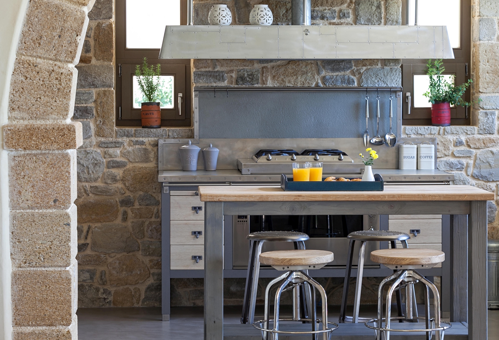 Kitchen with stone walls, table, stools, fresh juice and food, utensils and appliances at Villa Ianira on Crete, Greece