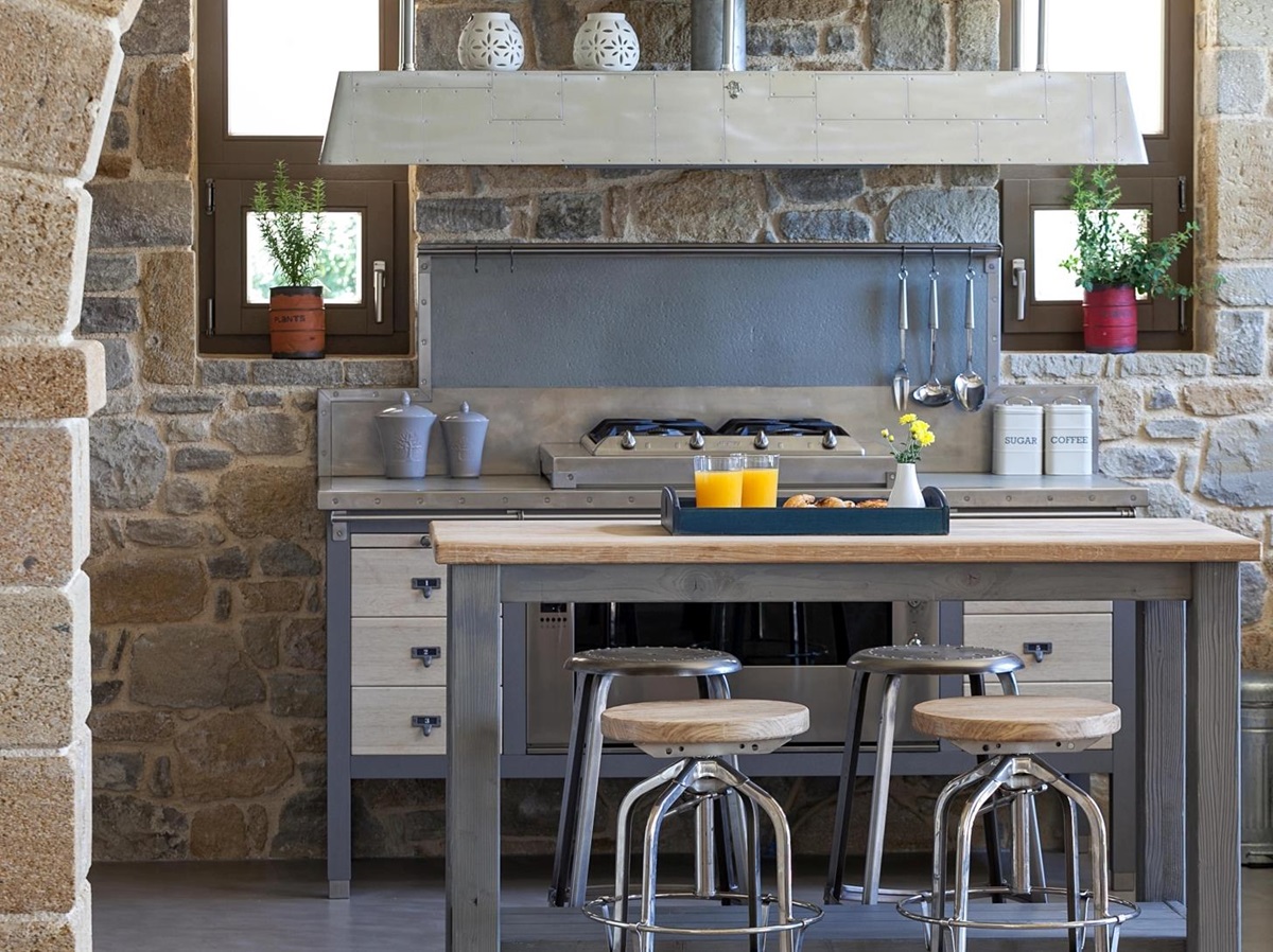Kitchen with stone walls, table, stools, fresh juice and food, utensils and appliances at Villa Ianira on Crete, Greece