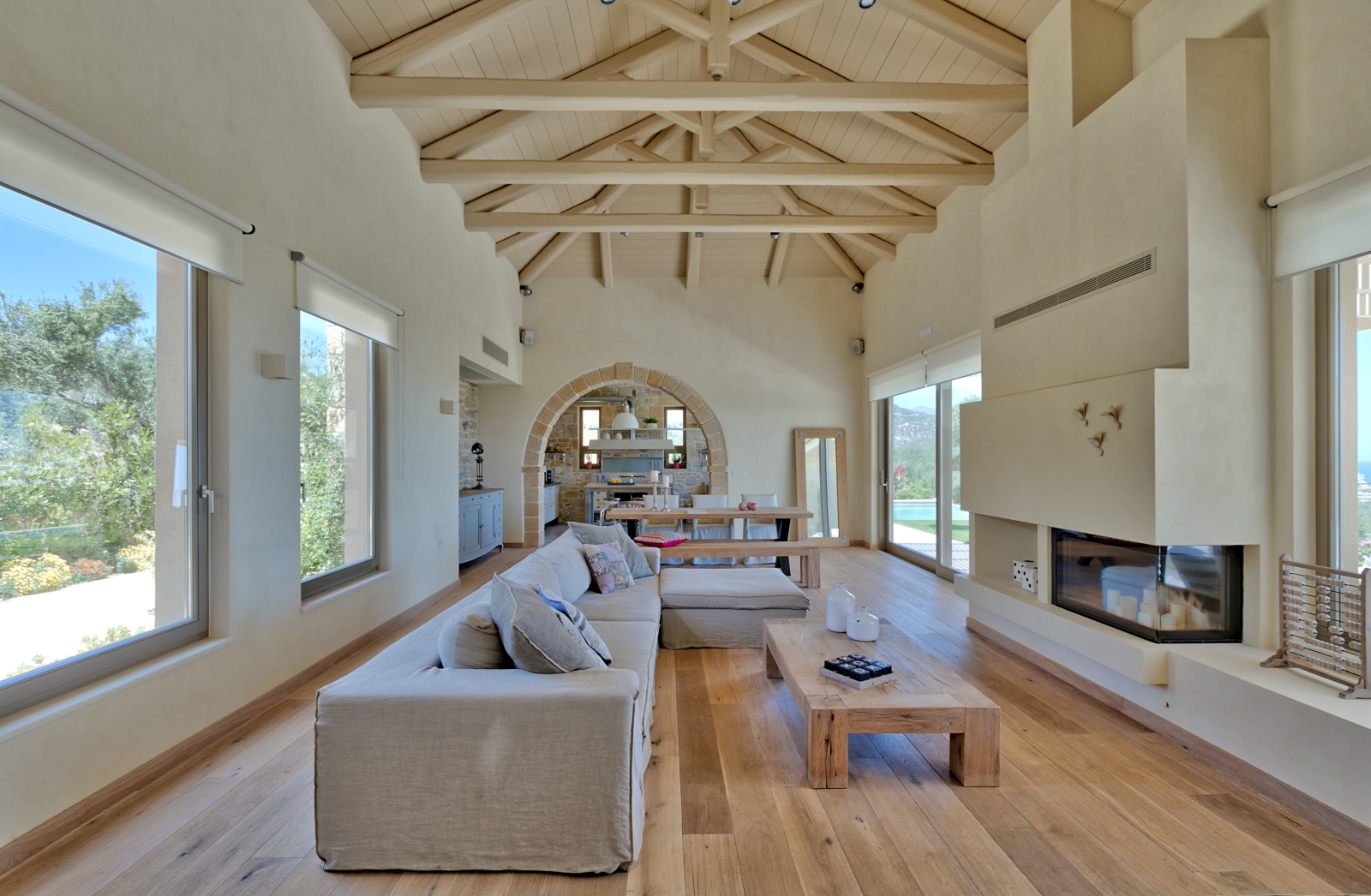Lounge with long sofa, coffee table, fireplace, large windows and view of dining area at Villa Ianira on Crete, Greece