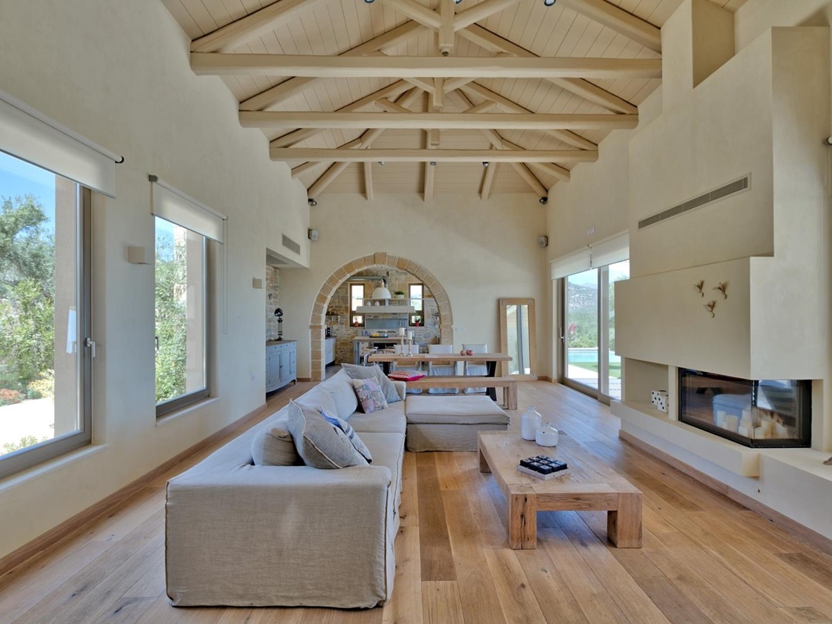 Lounge with long sofa, coffee table, fireplace, large windows and view of dining area at Villa Ianira on Crete, Greece
