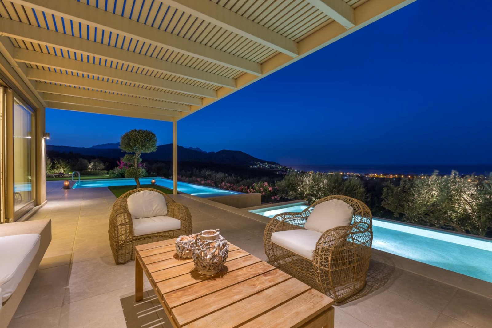 Covered outdoor lounge area with comfy chairs, coffee table, patio doors, pool and sea view at Villa Ianira on Crete, Greece