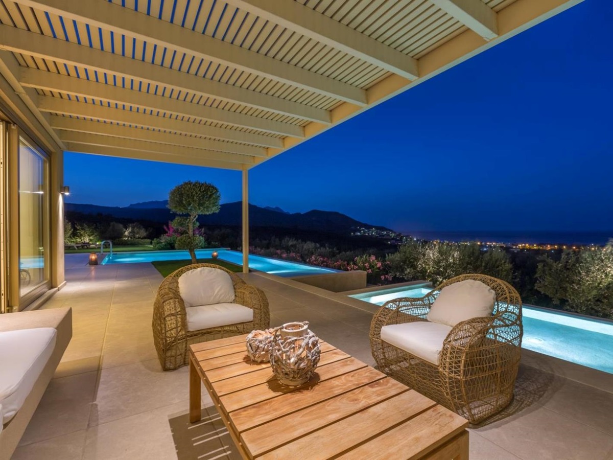 Covered outdoor lounge area with comfy chairs, coffee table, patio doors, pool and sea view at Villa Ianira on Crete, Greece