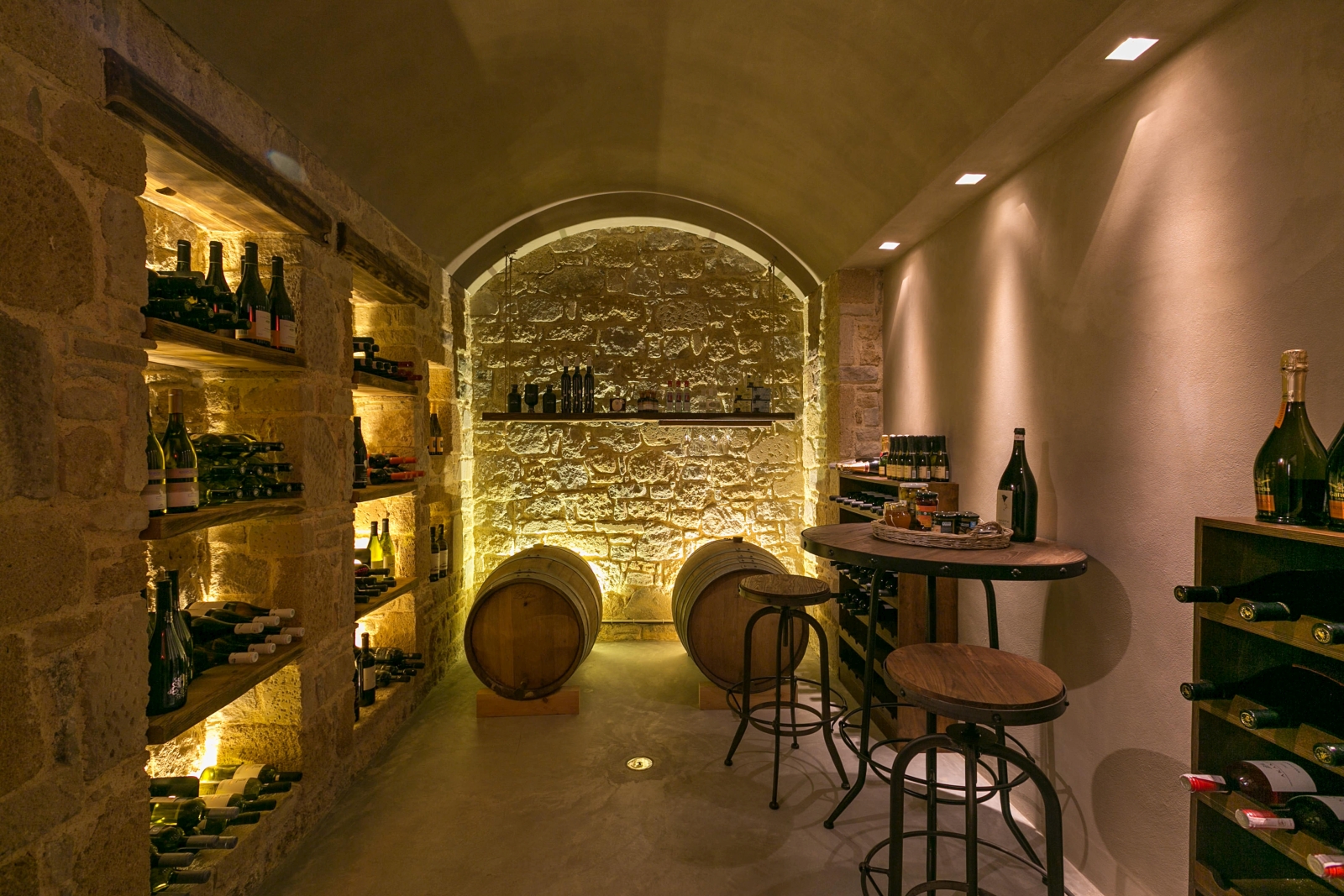 Wine cellar with stone walls, high table, stools, barrels, shelves and wine bottles at Villa Ianira on Crete, Greece