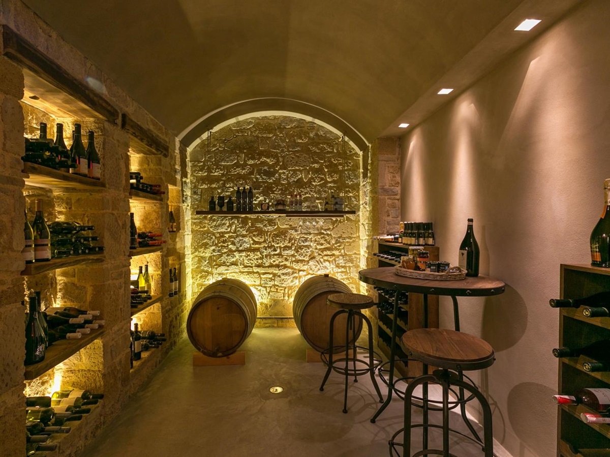 Wine cellar with stone walls, high table, stools, barrels, shelves and wine bottles at Villa Ianira on Crete, Greece