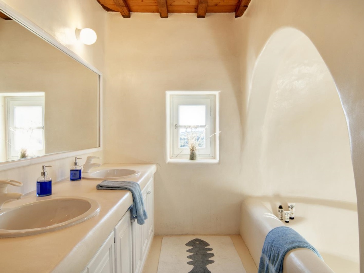 Bathroom with double sinks, large mirror, bath, and window at Villa Mari on Mykonos, Greece