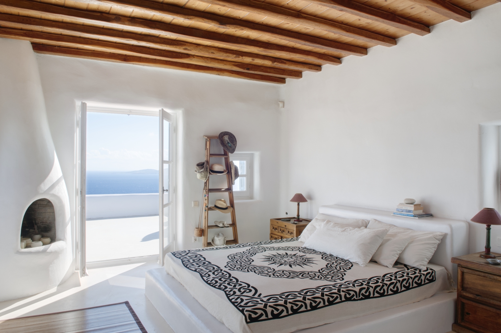 Bedroom with double bed, bedside tables, lamps, shelves and private terrace at Villa Mari on Mykonos, Greece