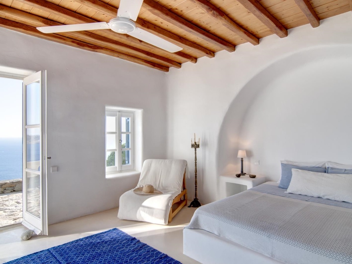 Bedroom with double bed, bedside table, lamp, armchair, ceiling fan and access to terrace at Villa Mari on Mykonos, Greece