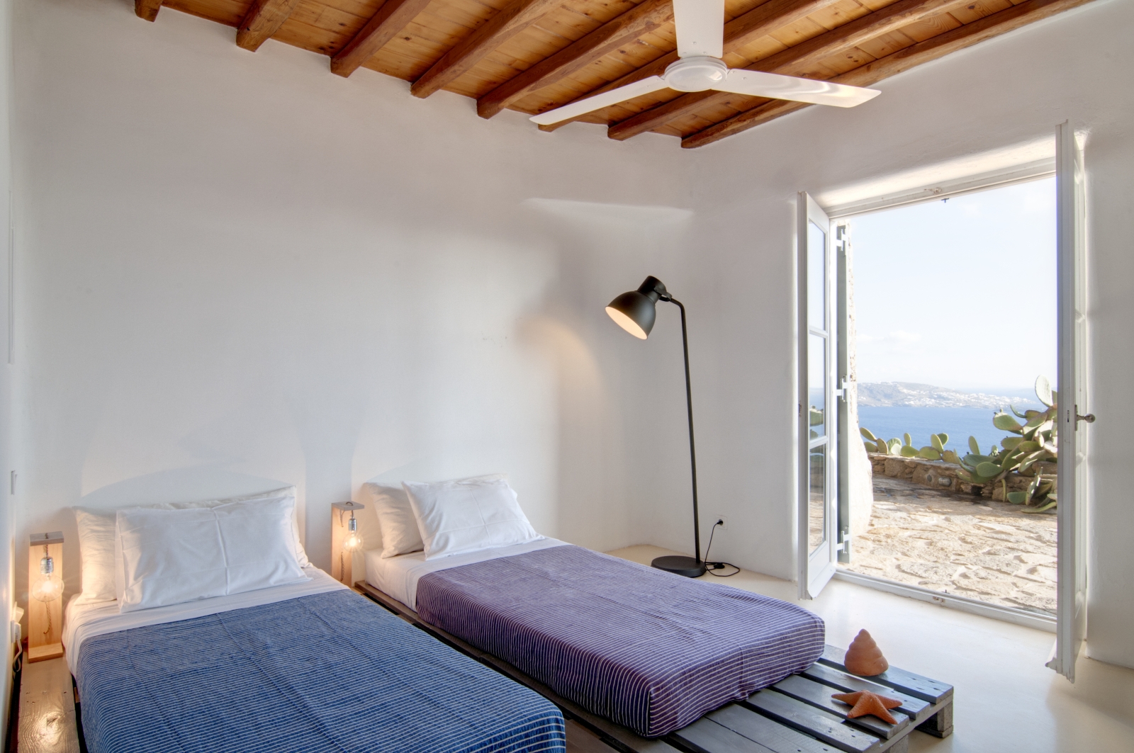 Bedroom with twin beds, lamp, ceiling fan and access to terrace at Villa Mari on Mykonos, Greece