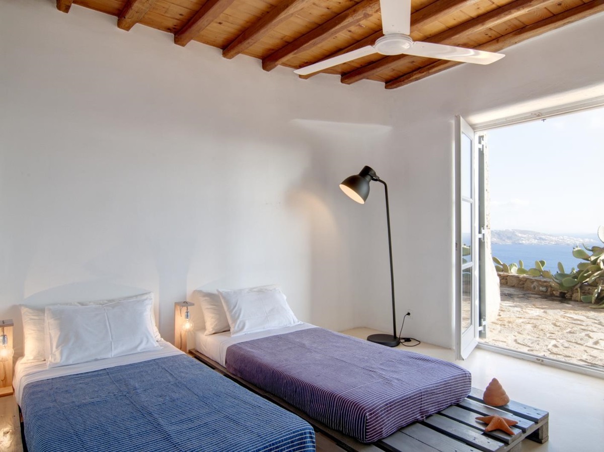 Bedroom with twin beds, lamp, ceiling fan and access to terrace at Villa Mari on Mykonos, Greece
