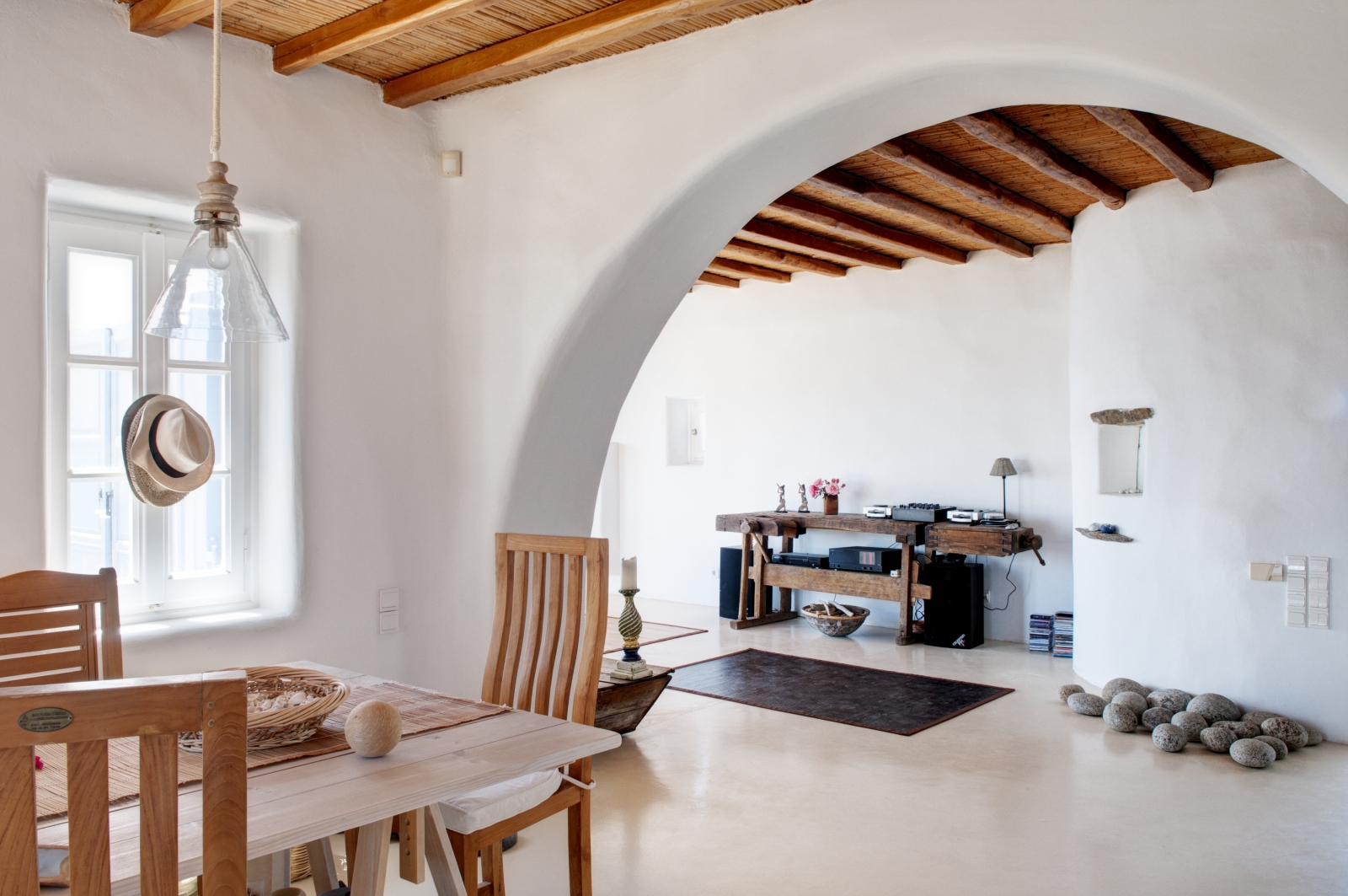 Living room and dining area with table, chairs, hanging light, archway and candle at Villa Mari on Mykonos, Greece