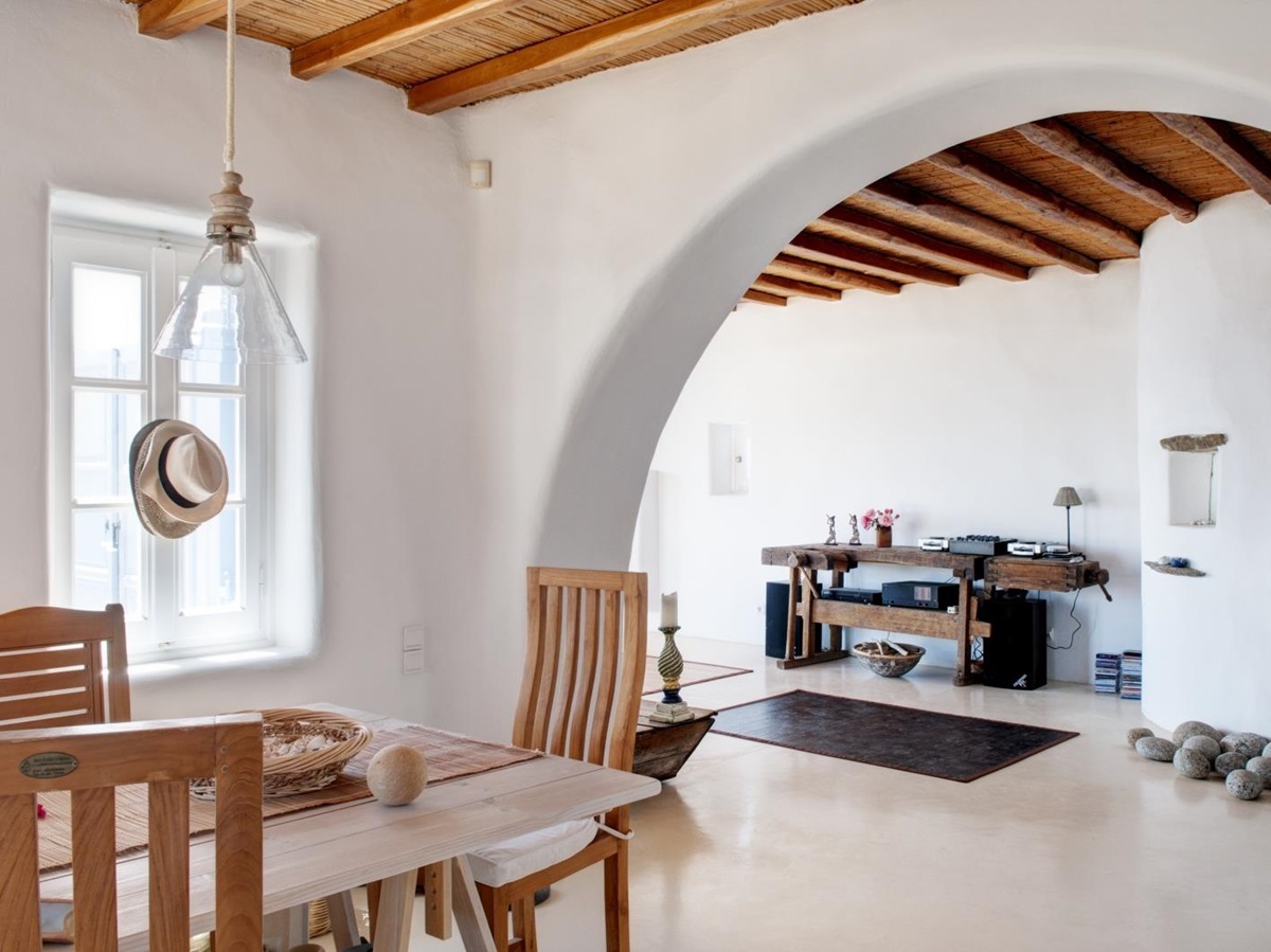 Living room and dining area with table, chairs, hanging light, archway and candle at Villa Mari on Mykonos, Greece