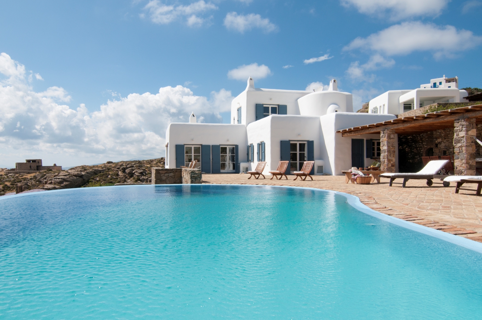 Façade of villa, infinity pool and terrace with sun loungers at Villa Mari on Mykonos, Greece