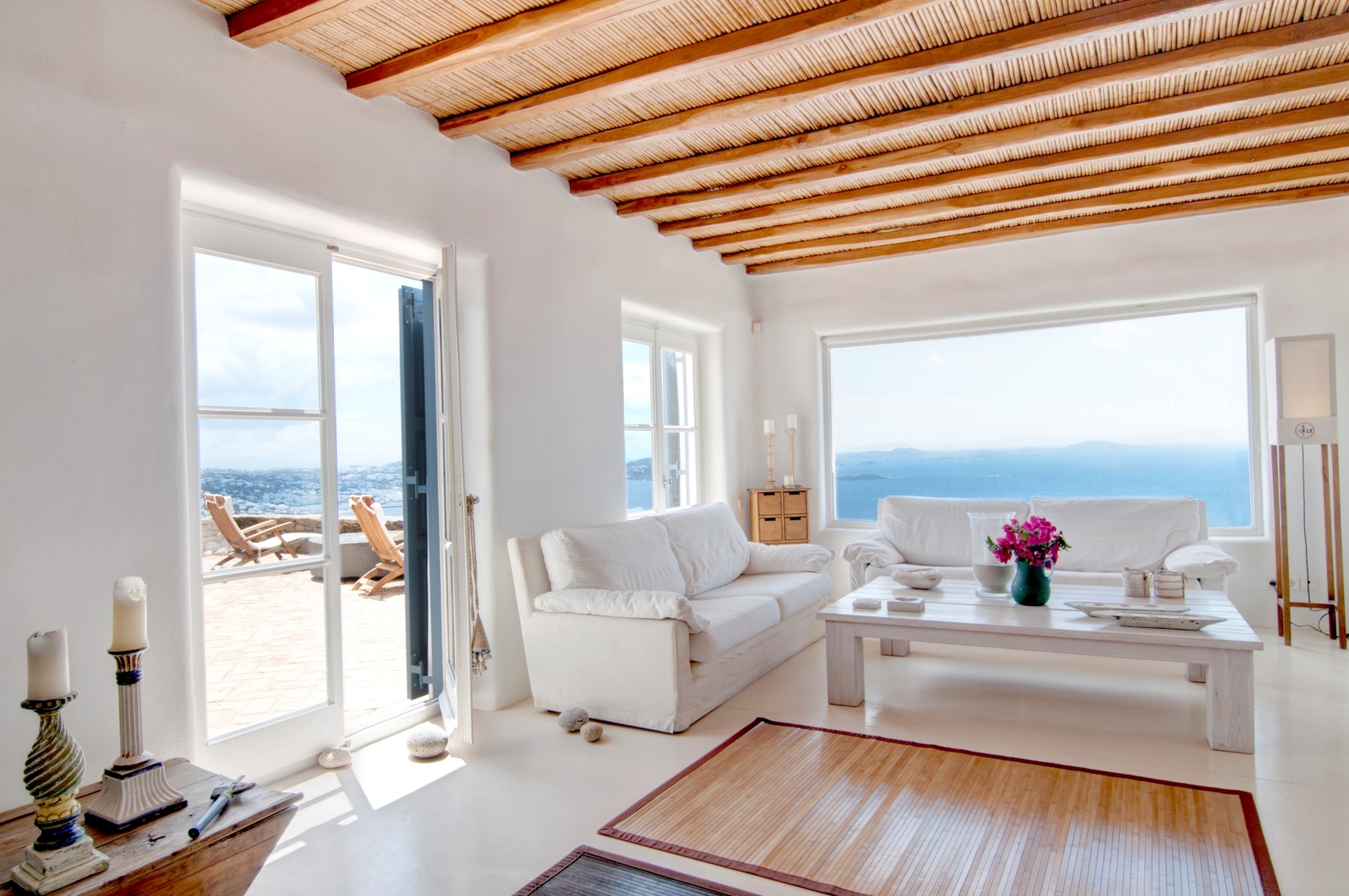 Living room with candles, sofas, coffee table, flowers, sea view and access to terrace at Villa Mari on Mykonos, Greece