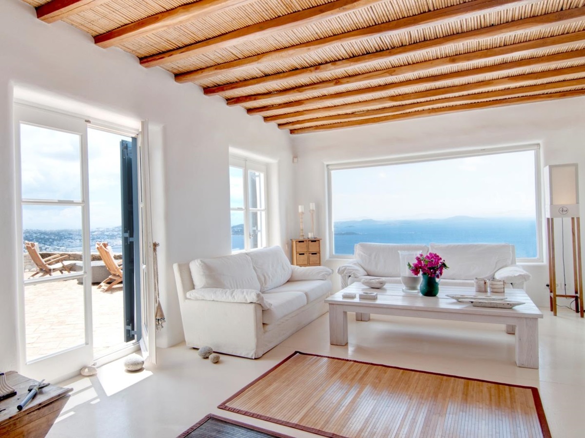 Living room with candles, sofas, coffee table, flowers, sea view and access to terrace at Villa Mari on Mykonos, Greece