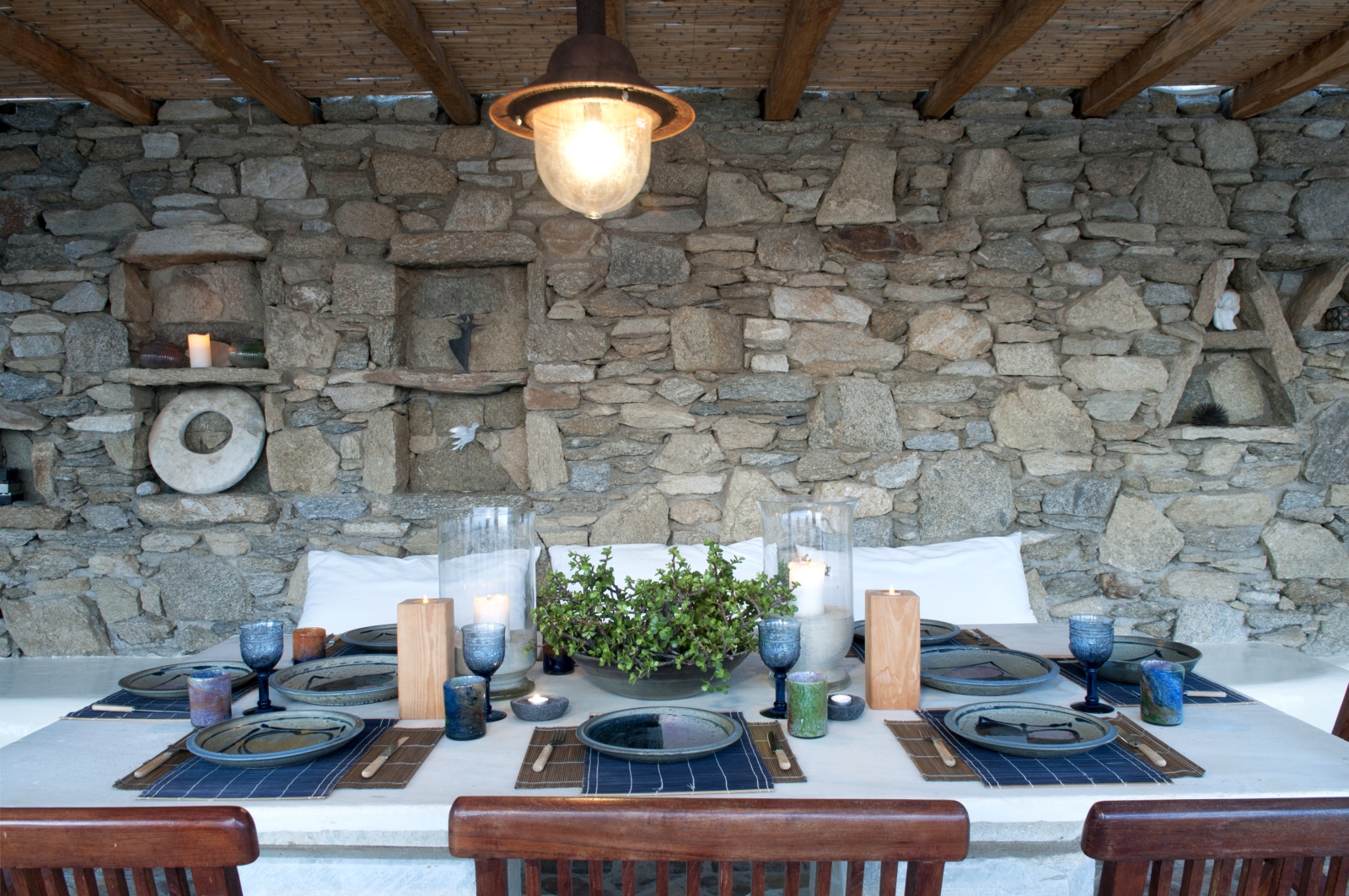 Outdoor dining area with hanging light, stone walls, candles, table and chairs at Villa Mari on Mykonos, Greece
