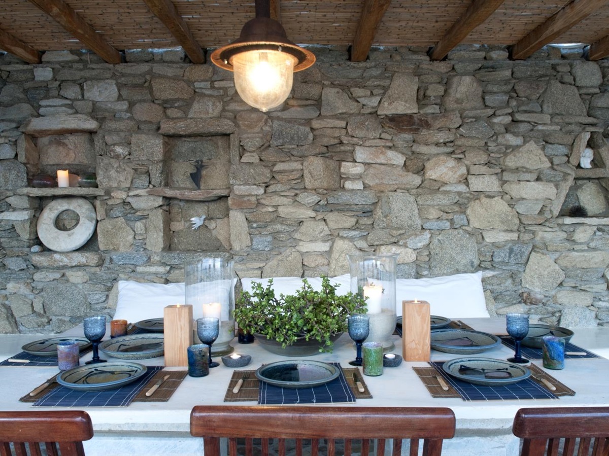 Outdoor dining area with hanging light, stone walls, candles, table and chairs at Villa Mari on Mykonos, Greece