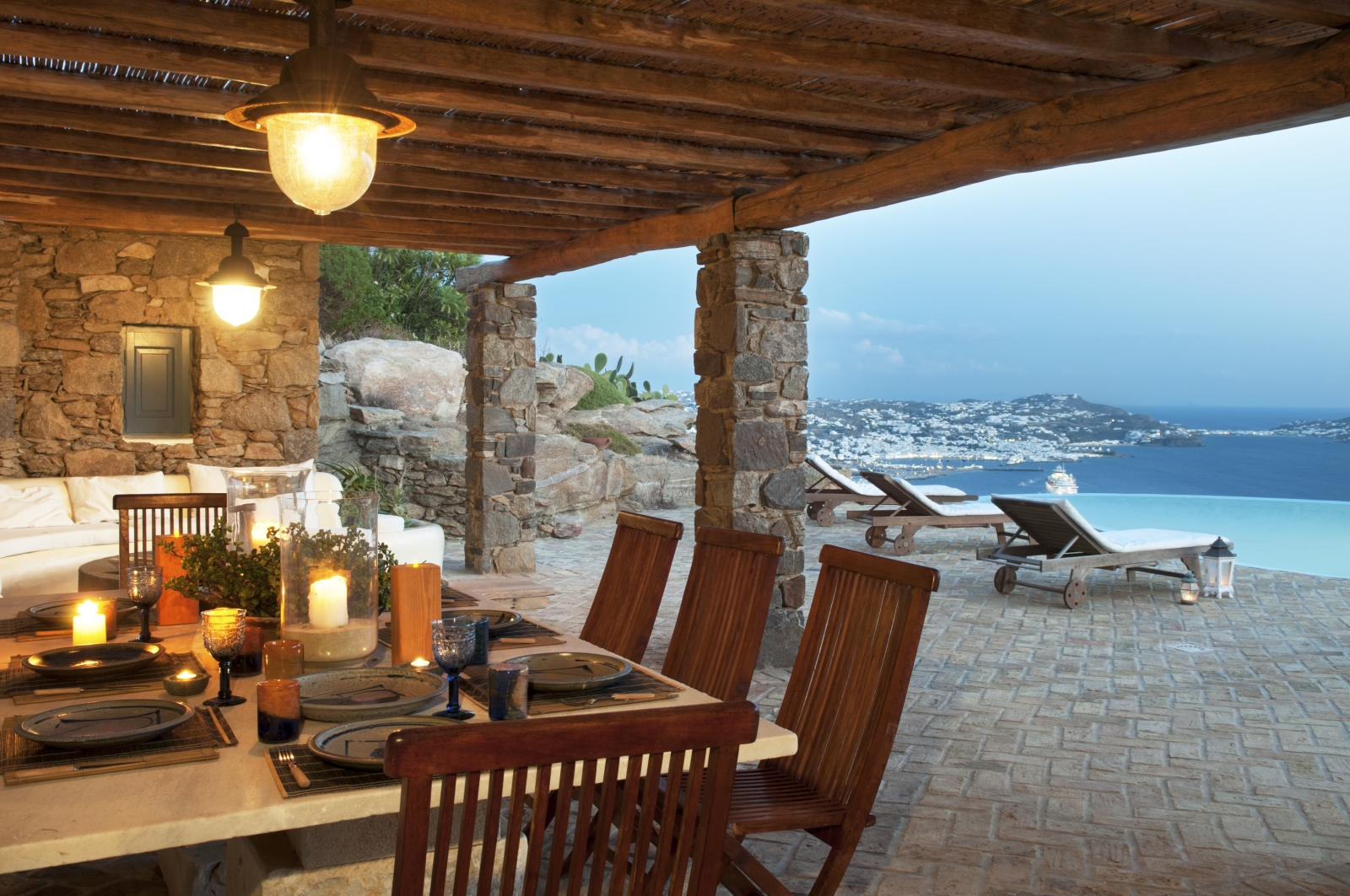 Covered outdoor dining area with set table, chairs, candles and sea view at Villa Mari on Mykonos, Greece