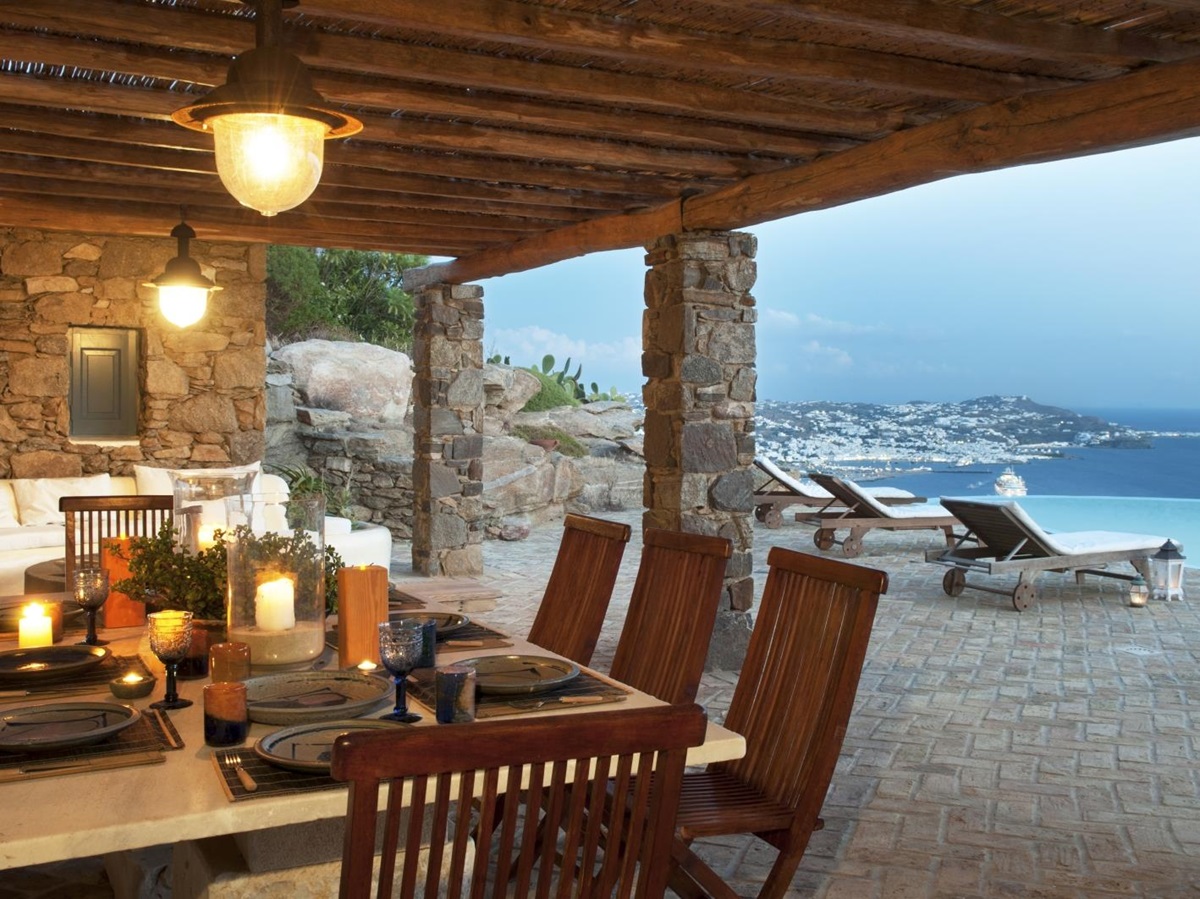 Covered outdoor dining area with set table, chairs, candles and sea view at Villa Mari on Mykonos, Greece