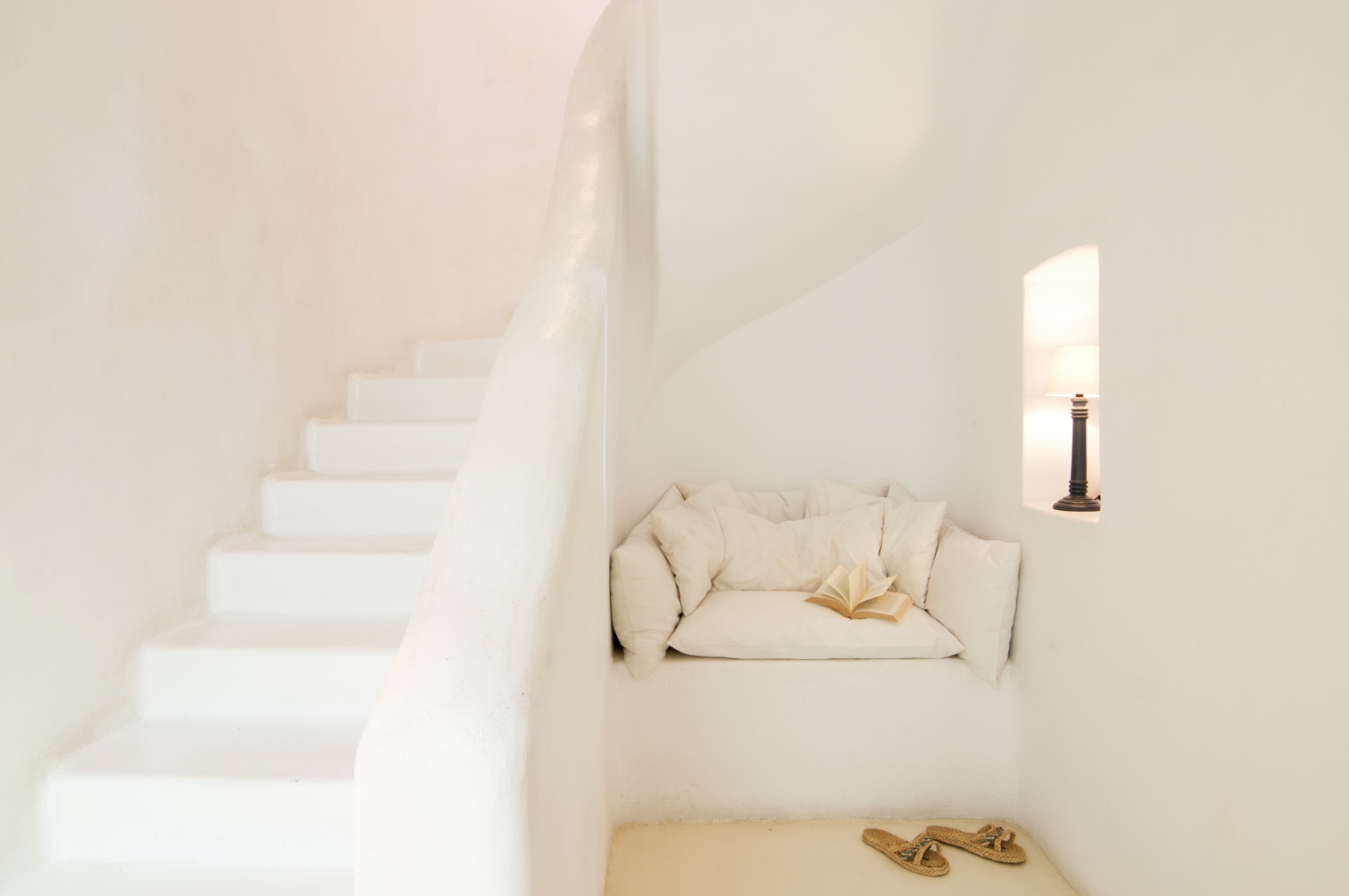 Reading corner next to staircase with cushions, book and candle at Villa Mari on Mykonos, Greece