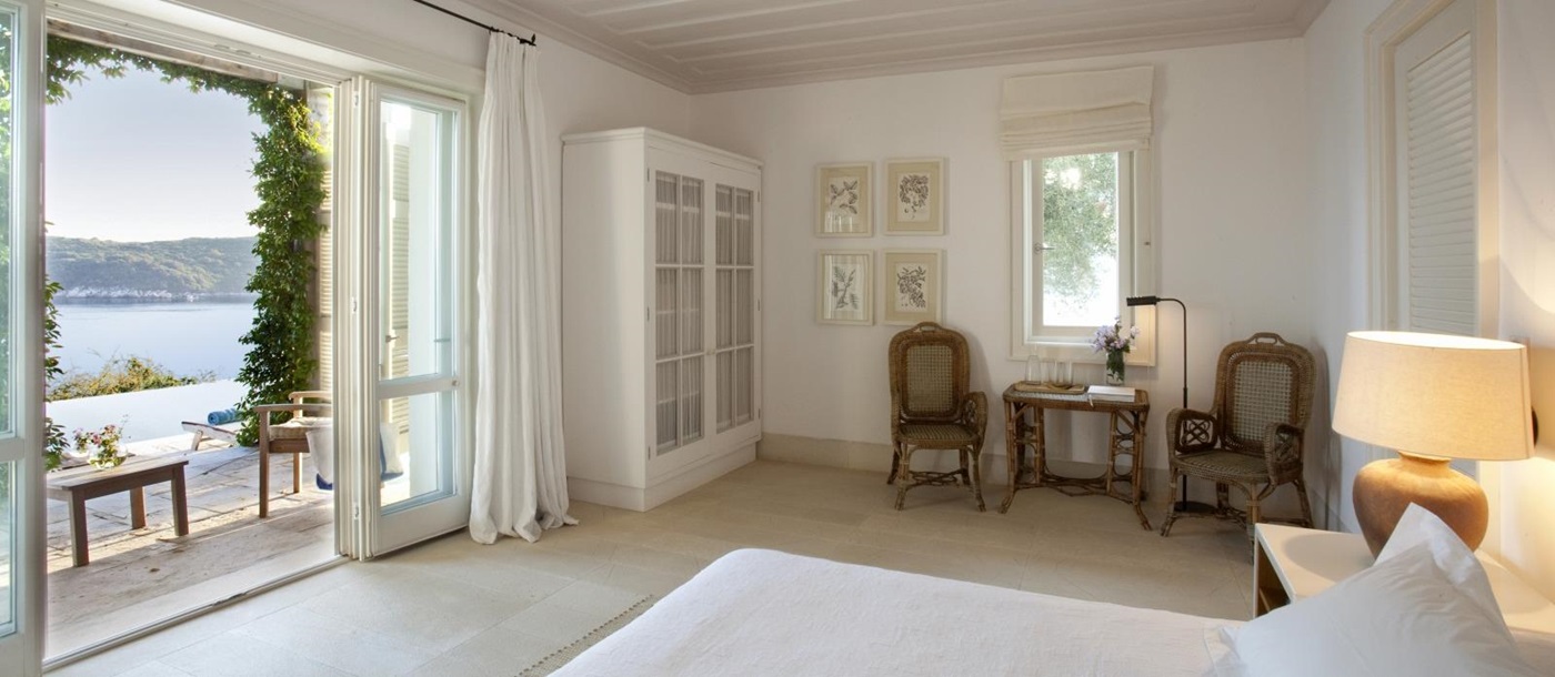 Bedroom with double bed, lamp, table, chairs, art, wardrobe, French doors & sea view at Villa Penelope on Corfu, Greece 