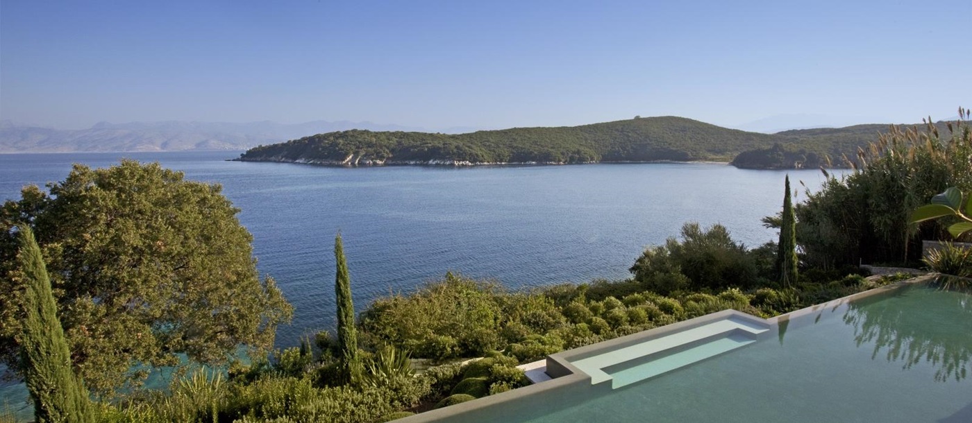 View of pool, trees, plants, sea and nearby headland at Villa Penelope on Corfu, Greece