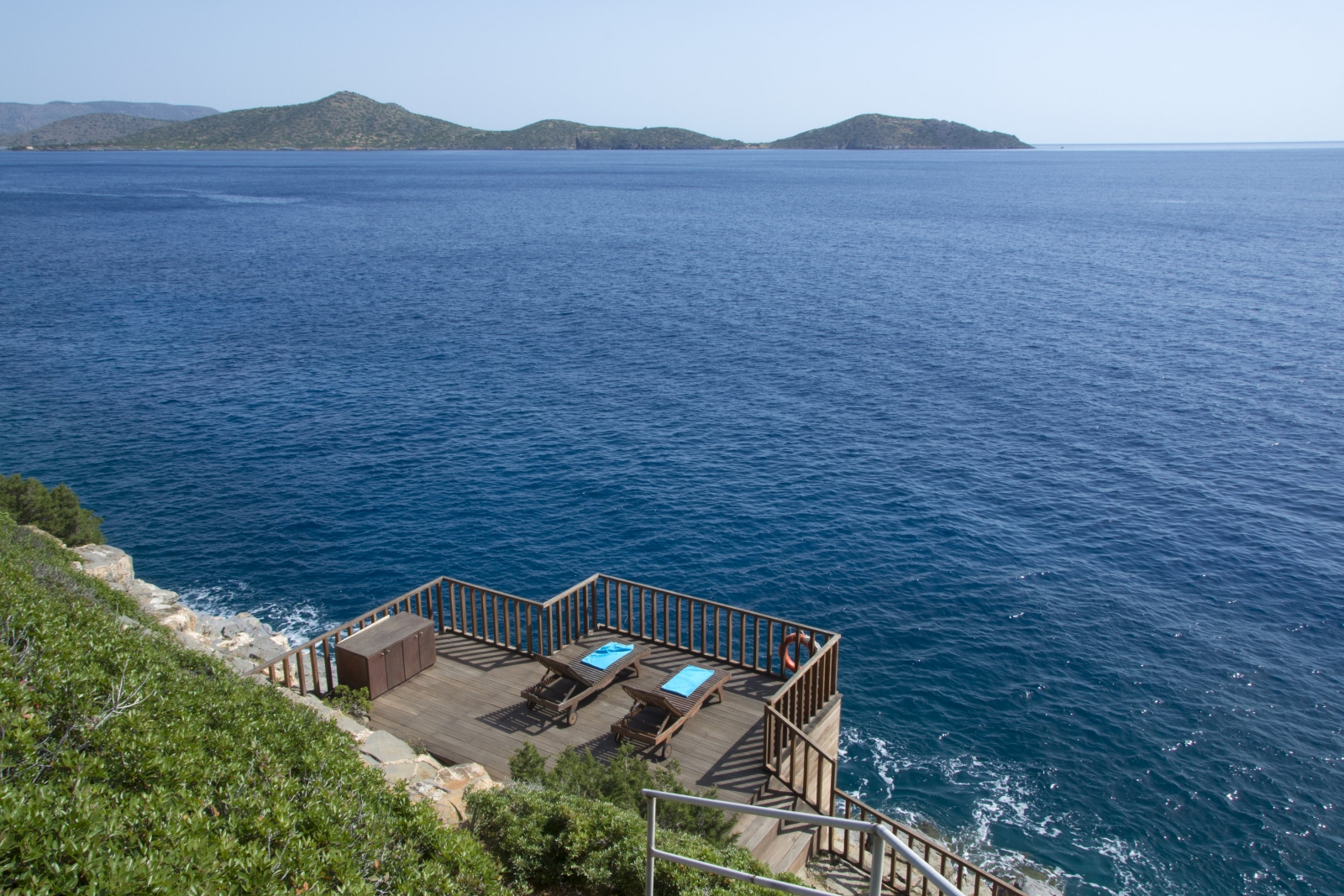 Decking with sun loungers and cabinet by sea below Villa Selene on Crete, Greece