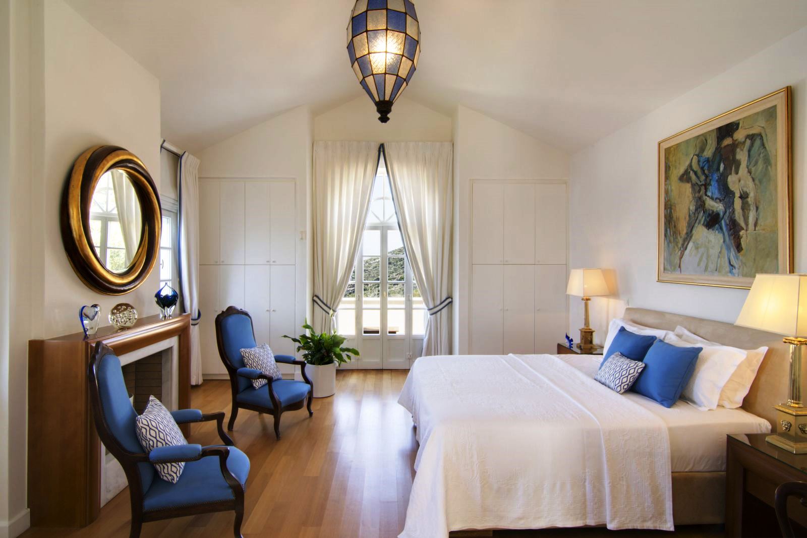 Double bedroom with wooden floor, glass doors out onto a balcony and blue chairs and big picture over the bed at Villa Selene in Crete