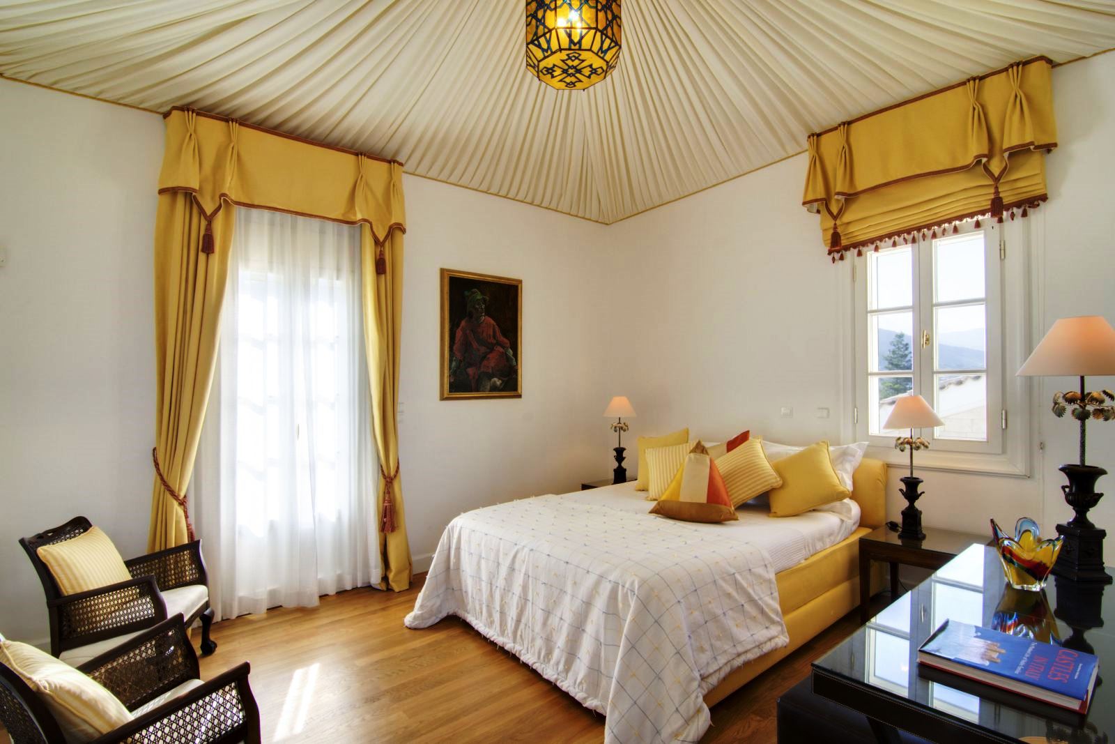 Double bedroom with wooden floor, two windows and yellow furnishings Double bedroom with wooden floor