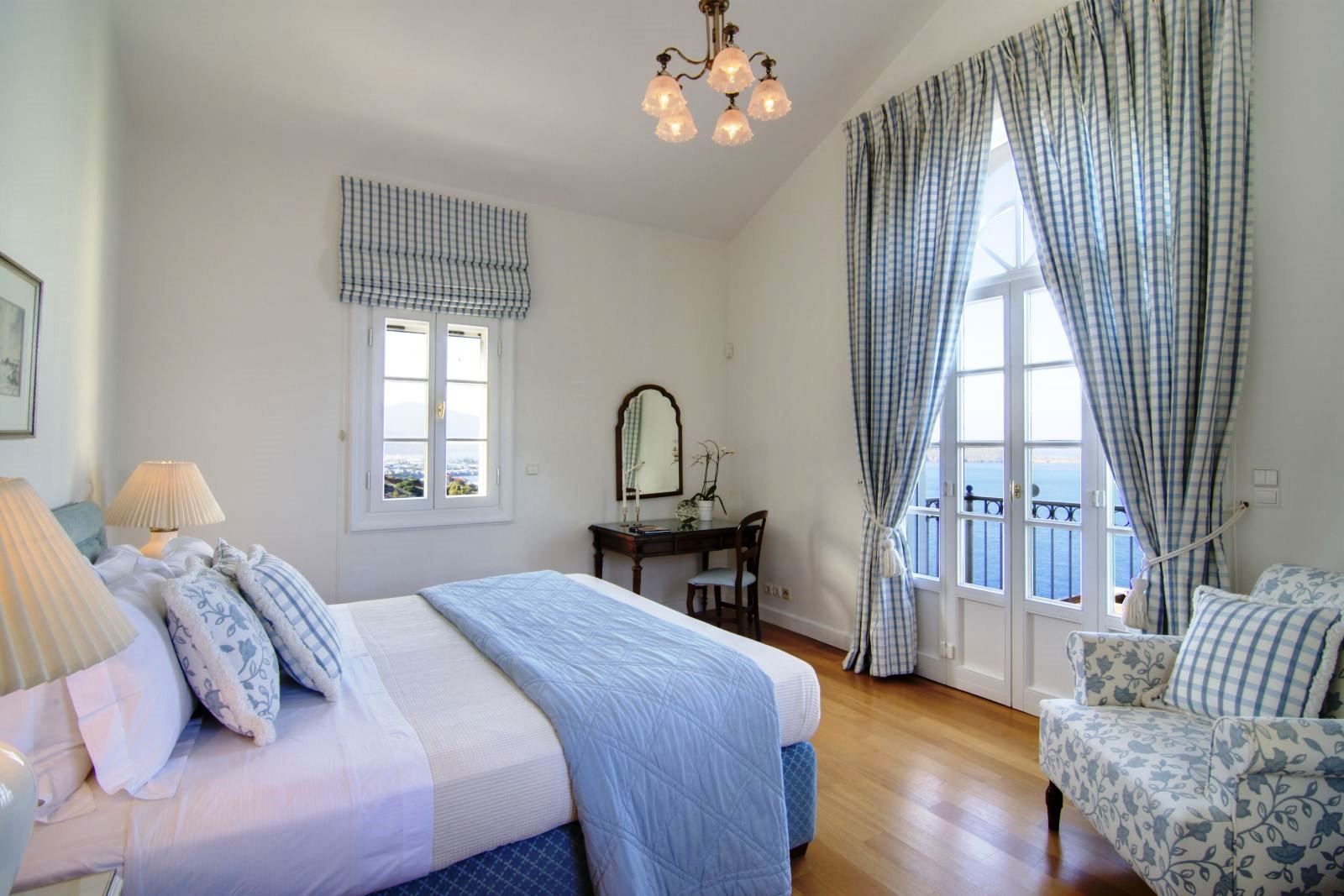 Small double bedroom with blue furnishings, wooden floor, window and glass door out onto a balcony overlooking the sea at at Villa Selene in Crete