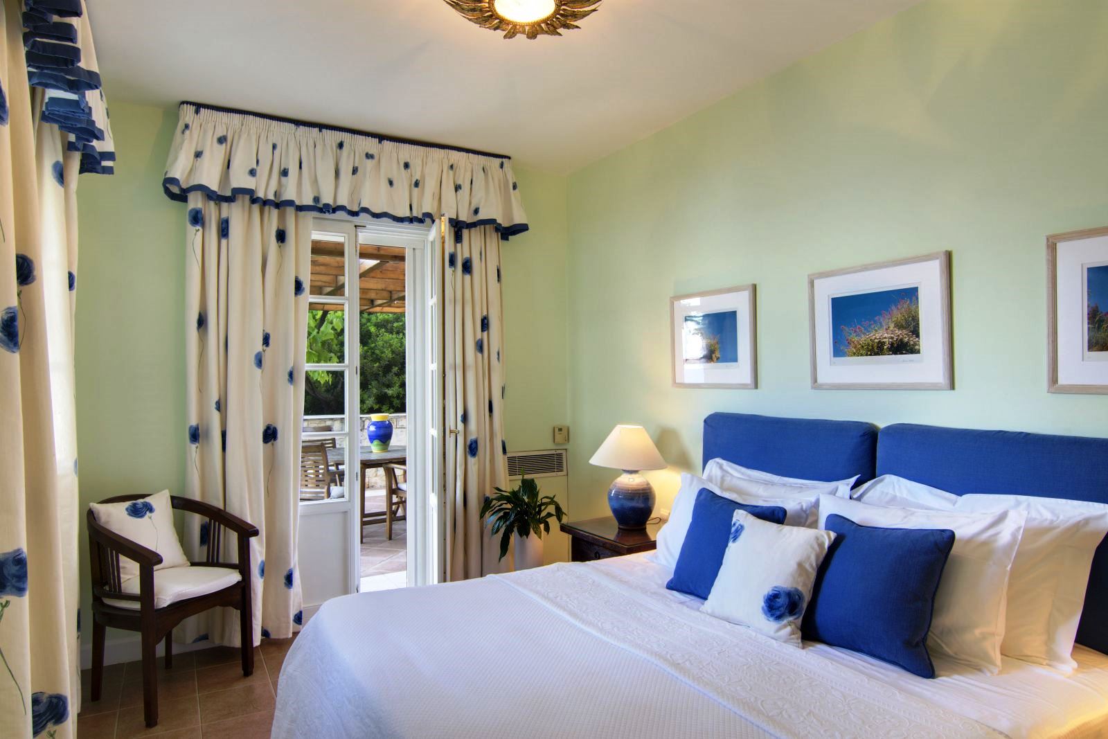 Double bedroom with pale green walls and blue flowered furnishings and open glass door out onto a terrace at Villa Selene in Crete
