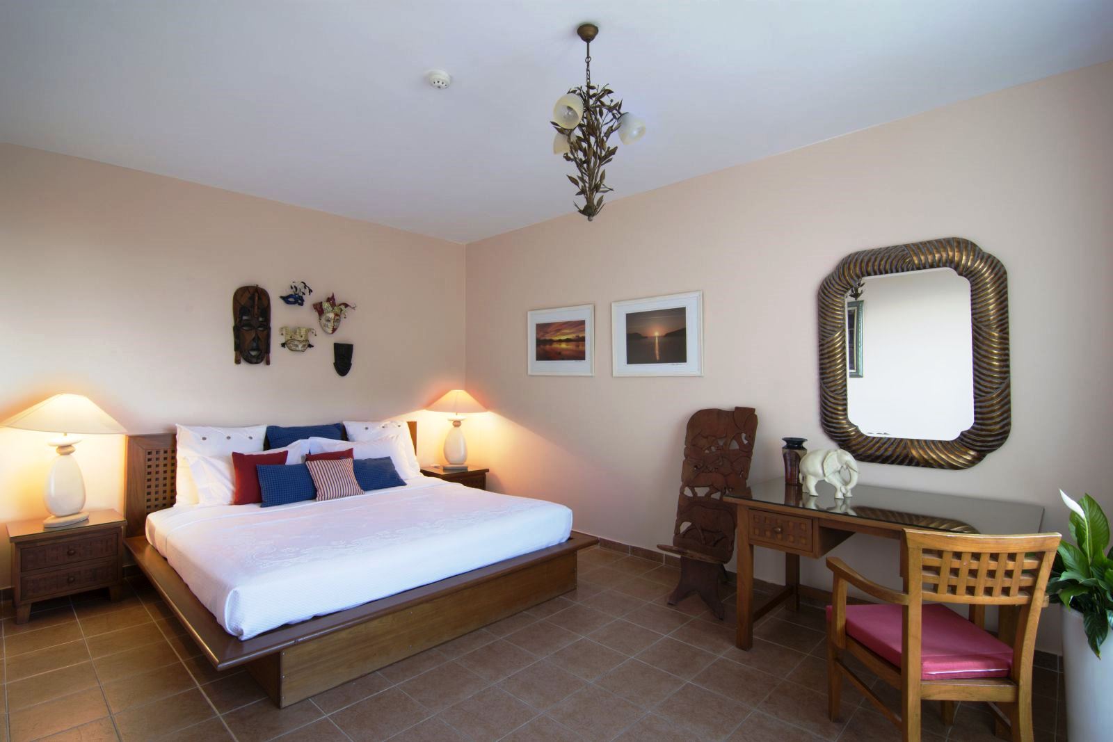 Double bedroom with brown tiled floor and wooden furnishings and modern bed with blue and red cushions at at Villa Selene in Crete
