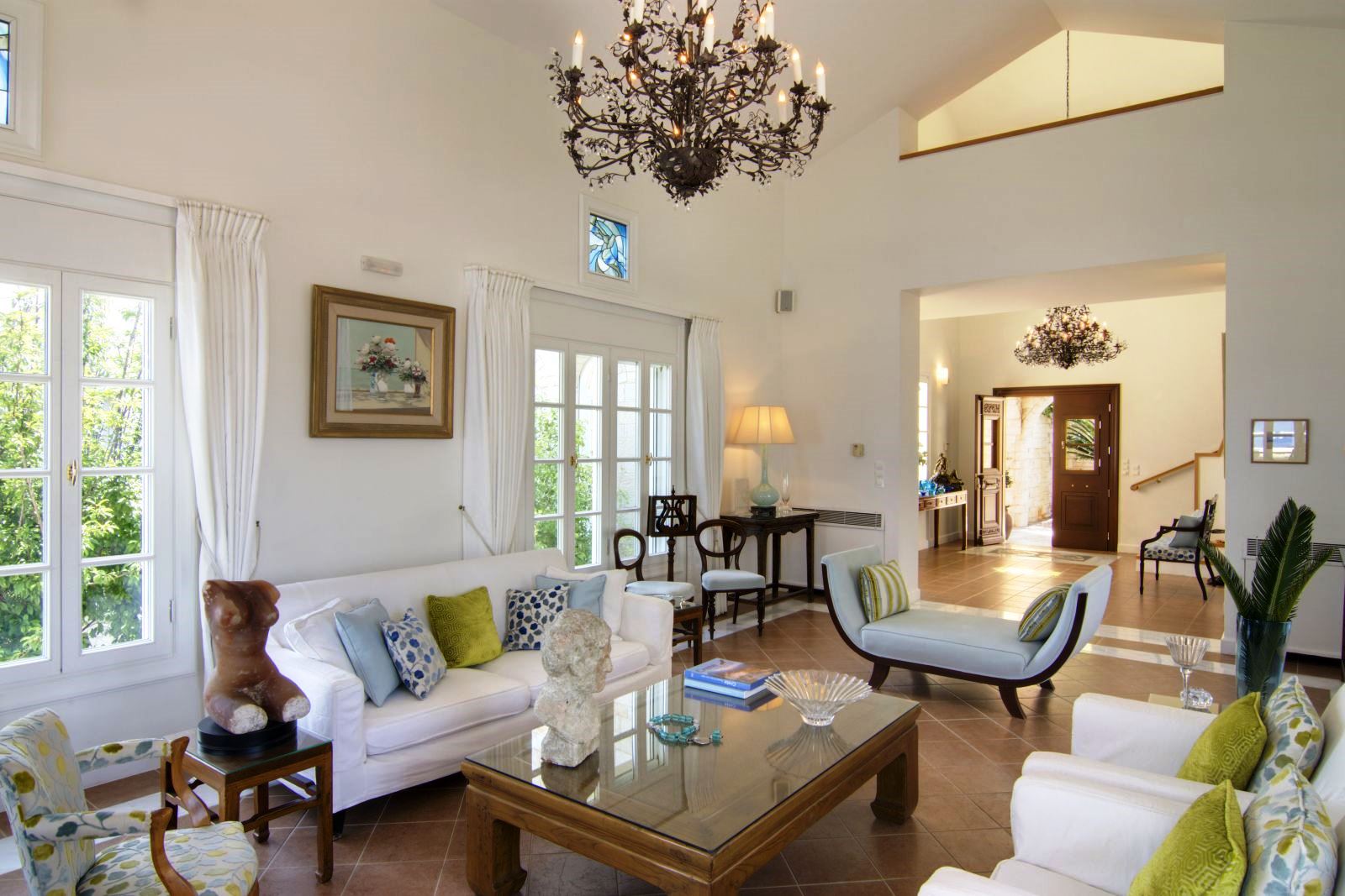 Seating area with brown tiled floor and white sofa and chairs with green and blue cushions at Villa Selene in Crete