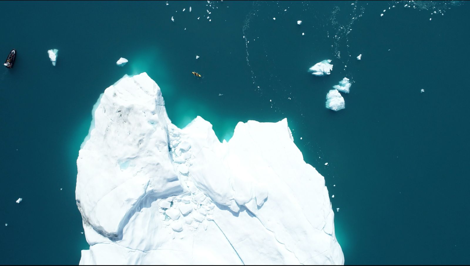 Aerial view of travellers kayaking around an iceberg in Arctic Greenland