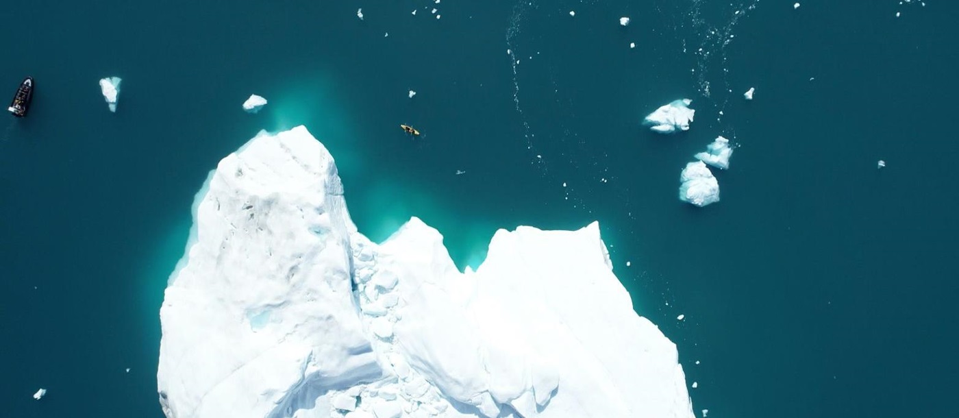 Aerial view of travellers kayaking around an iceberg in Arctic Greenland