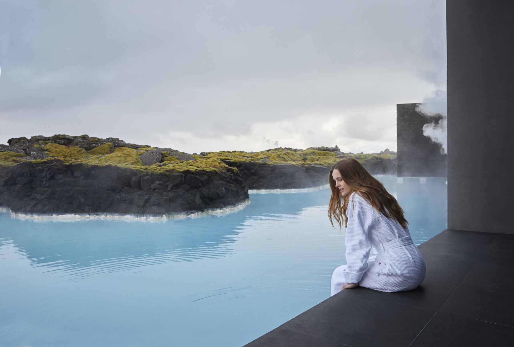 Lady dipping her feet into thermal waters from her room at The Retreat at Blue Lagoon hotel in Iceland