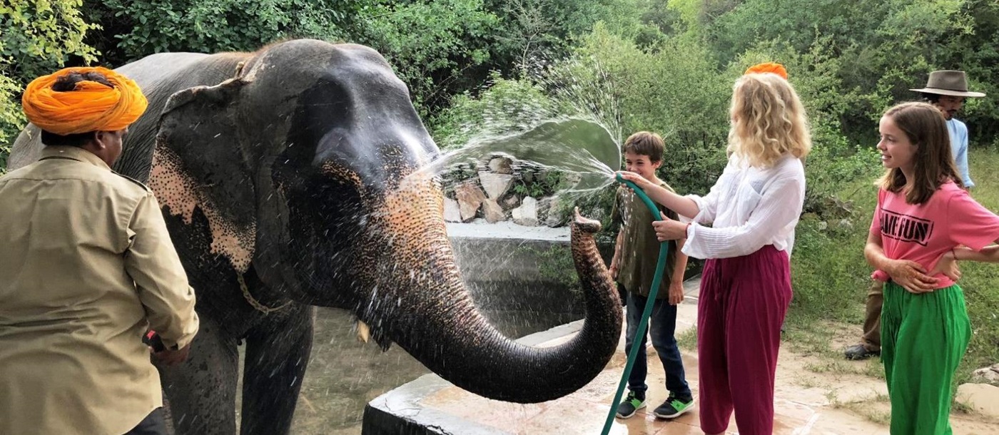 A lady and two children washing an elephant with a hose pipe in India
